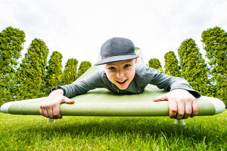 Young boy hanging down on raised hammock chair in the green garden.の写真素材