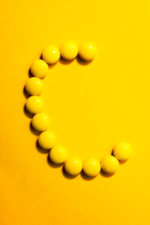 Top view of  letter C made of yellow pills on yellow background. Medicine Vitamin C concept.の写真素材