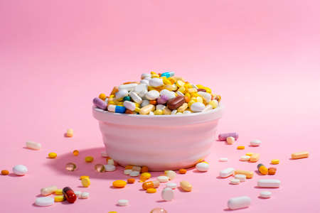 Bowl full of colorful pills on pink background. Creative composition.の写真素材