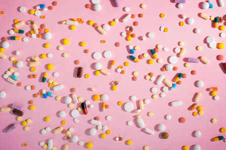 Background with medicines, pills, supplements and vitamins tablets on pink background.