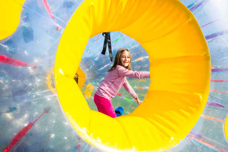 Young girl has a lot of fun in the inflatable cylinder of Zorbing Ball, outdoor in the park.
