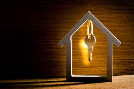 Silver key hanging inside white house on vintage wooden background with light reflection. Concept for real estate, moving home or renting property.の写真素材