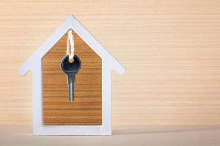 Silver key hanging inside white house on vintage wooden background. Concept for real estate, moving home or renting property.の写真素材