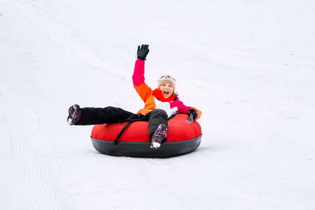 Child girl on snow tubes downhill at winter day.の写真素材