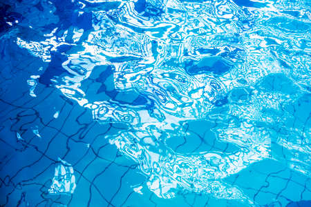 Blue swimming pool rippled water detail with sunny reflection.