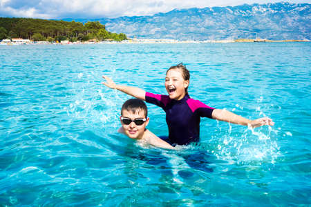 Boy and girl splashing in the water and playing in the ocean while on vacation. Croatia.の写真素材