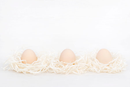 Raw organic three brown eggs in nest made of staw shreded paper.の写真素材