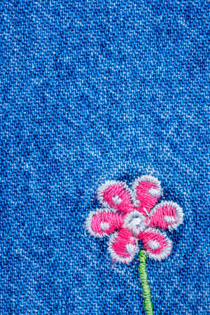 Embroidered pink flower on fragment of blue denim jeans texture
