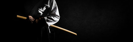 A person in black hakama standing in fighting pose with wooden sword bokken over grunge dark background banner. Shallow depth of field. SDF.の写真素材