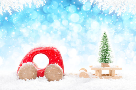 Red Wooden Car Pulling Sled with A Christmas Tree in perspective on bright blue bokeh winter background with white snowy branches and falling snow.の写真素材