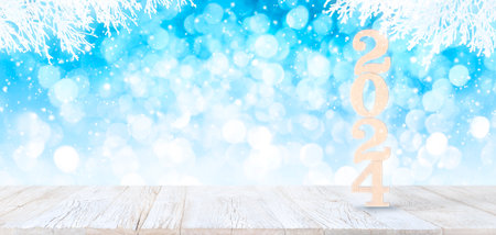 Happy New Year 2024 Wooden Numbers on white vintage planked wood table in perspective on bright blue bokeh winter background with white snowy branches and falling snow.の写真素材