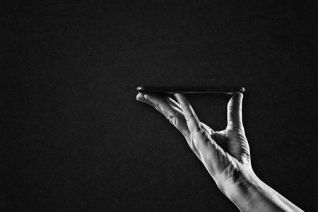 Hand in Black and White Holding Smartphone on Textured Paper Background, Copy Space