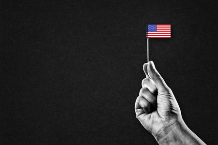 Hand in Black and White Holding an American Flag, Black Textured Background with Copy Spaceの写真素材