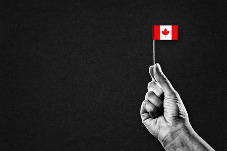 Hand in Black and White Holding Canada Flag, Black Textured Background with Copy Spaceの写真素材