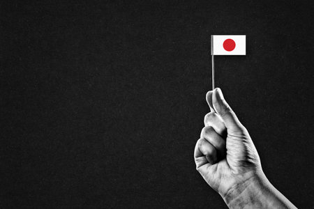 Hand in Black and White Holding Japanese Flag, Black Textured Background with Copy Spaceの写真素材