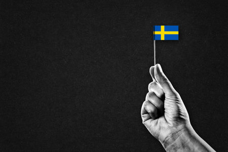 Hand in Black and White Holding Swedish Flag, Black Textured Background with Copy Spaceの写真素材