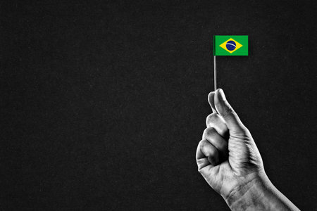 Hand in Black and White Holding Brazil Flag, Black Textured Background with Copy Spaceの写真素材