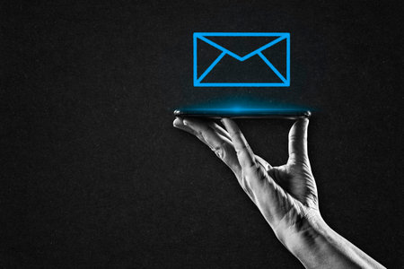 Hand in Black and White Holding Smartphone with Blue Email Sign on Textured Paper Background, Copy Spaceの写真素材
