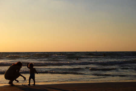 young woman with small child on the sea shore on sunsetの写真素材