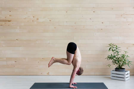 Sporty man practices yoga handstand asana Adho Mukha Vrikshasana at the yoga studio. Balance exerciseの写真素材