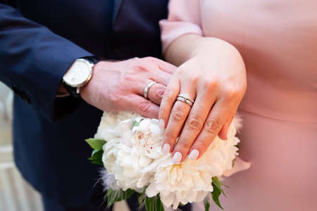 Hands of the groom and bride with rings and bridal bouquetの写真素材