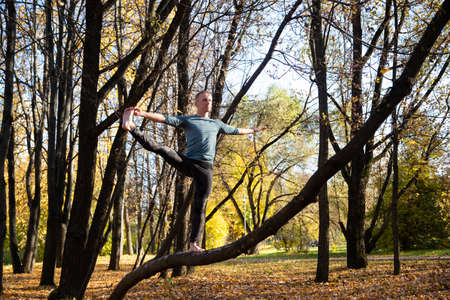 Sporty man practicing yoga in autumn park