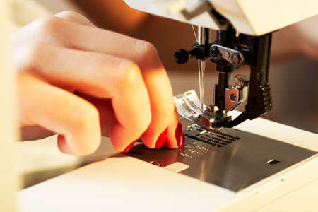 A hand of a dressmaker supporting a cloth while sewing on a sewing machine 