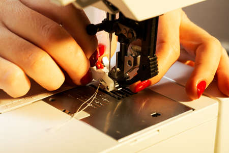 A hand of a dressmaker supporting a cloth while sewing on a sewing machine 