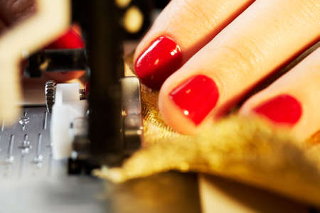 A hand of a dressmaker supporting a cloth while sewing on a sewing machine の写真素材