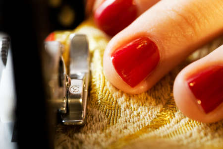 A hand of a dressmaker supporting a cloth while sewing on a sewing machine の写真素材