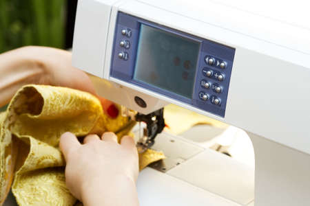 A hand of a dressmaker supporting a cloth while sewing on a sewing machine 