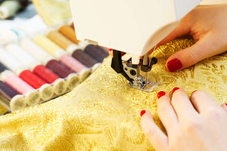 A hand of a dressmaker supporting a cloth while sewing on a sewing machine 