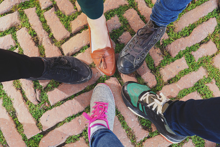 Legs of five friends in different shoes standing together, top view