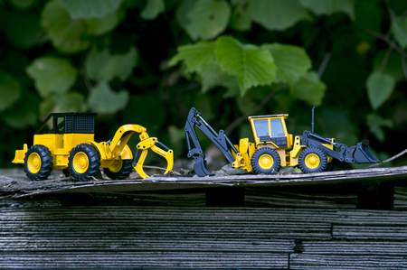 Two forklift toy cars on a wide wooden plank stimulate our concentricity.の写真素材