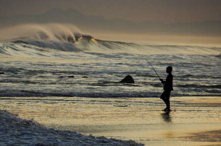 A young boy fishing in the rough surf at sunset の写真素材