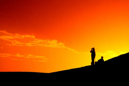 Beautiful orange sky with a silhouetted couple watching の写真素材