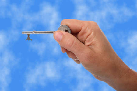 Woman's hand holding a silver key in her fingers and blue sky backgroundの写真素材