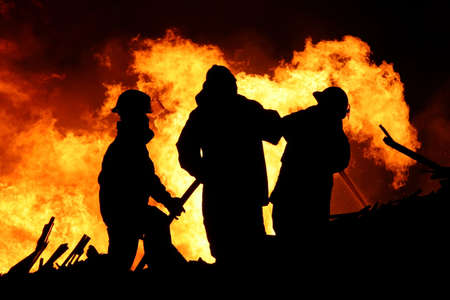 Three firemen fighting a raging fire with huge flames of burning scrap timberの写真素材