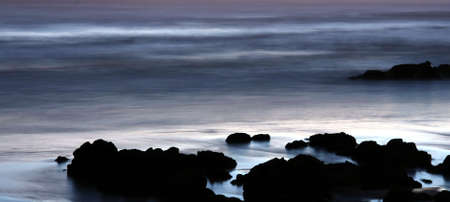 Rocks on the seashore at dusk with moving sea waterの写真素材