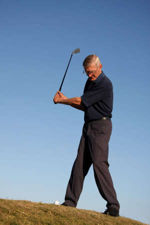 Senior golfing man about to strike the ball in the fairwayの写真素材