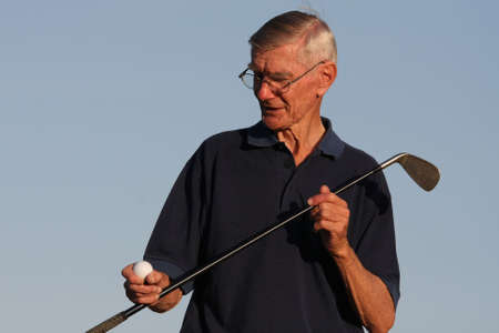 Elderly golfer inspecting his golf ball and clubの写真素材