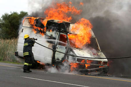 Fireman spraying water into a burning van on a roadの写真素材