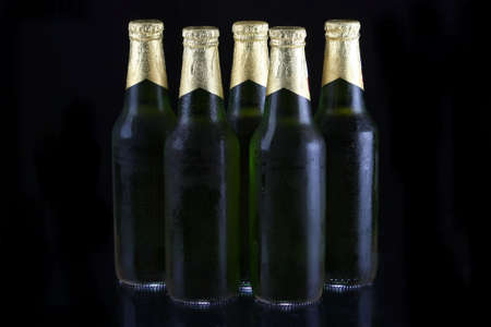 Green beer bottles with gold foil tops against black backgroundの写真素材