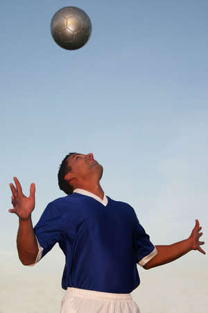 Soccer player in blue shirt heading the ballの写真素材