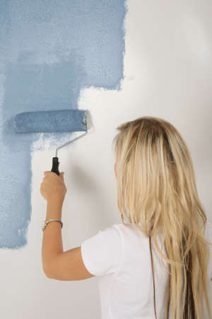 Young blond woman home owner painting a wall blueの写真素材