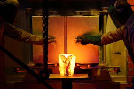 Two men working in protective clothing to pour gold