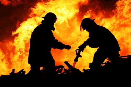 Silhouette of Firemen fighting a raging fire with huge flames of burning timberの写真素材
