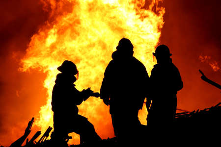 Three firemen fighting a raging fire with huge flames of burning  timber