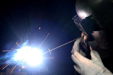 Welder with protective gloves and helmet welding steel