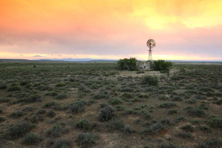 Wide open farm land with a water windmill pump at sunset in the Karoo in South Africaの写真素材